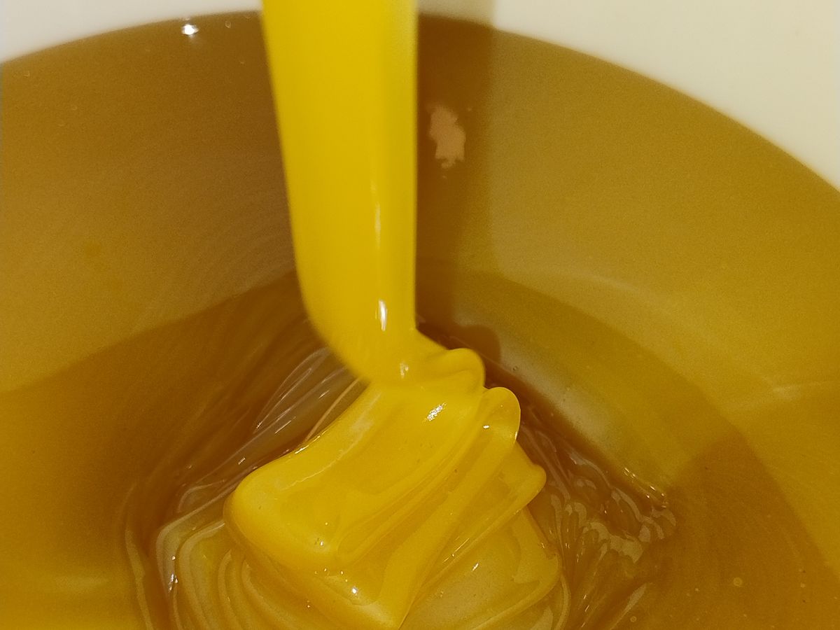 Honey with a naturally thick, pale texture being poured before jarring